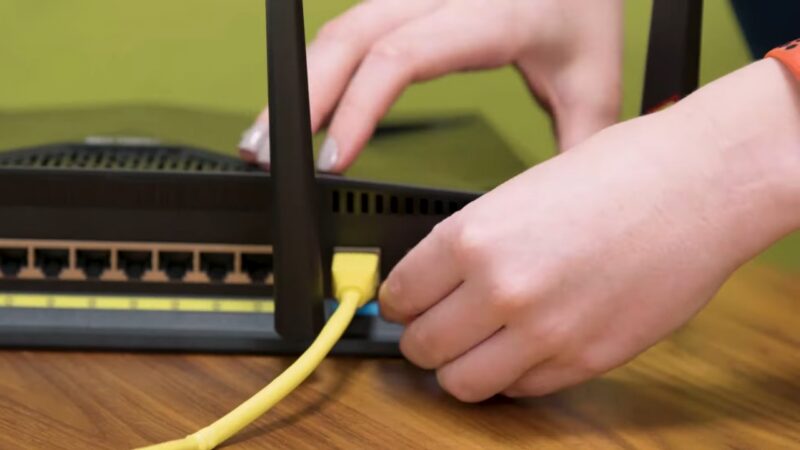 A Person Is Unplugging a Yellow Ethernet Cable from The Back of A Modem or Router, Preparing to Disconnect the Device