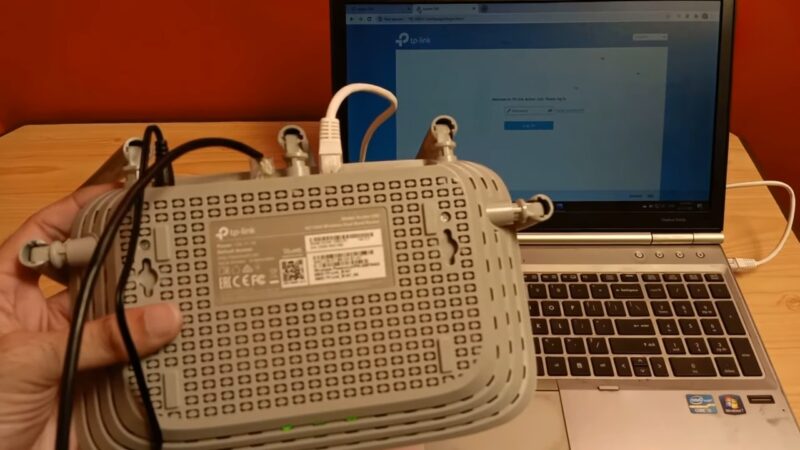 A Person Is Holding a TP-Link Modem Connected to A Laptop, with The Laptop Screen Displaying the Modem's Software Setup Interface for Configuration