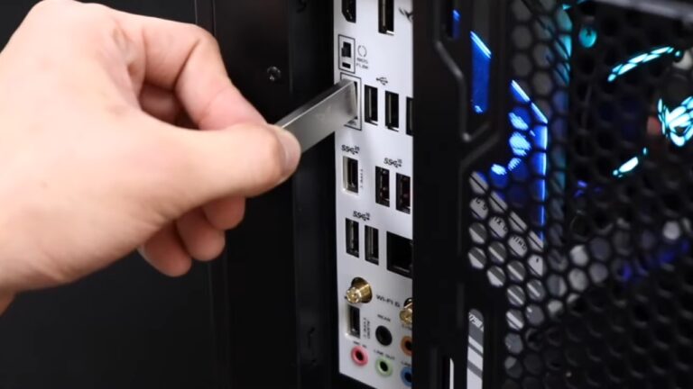 The Image Shows a Person Inserting a USB Flash Drive Into a USB Port on The Back Panel of A Computer Case, Likely to Perform a USB BIOS Flashback